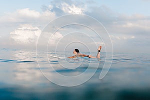 Young woman in bright bikini surfing on a board in ocean