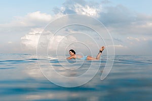 Young woman in bright bikini surfing on a board in ocean