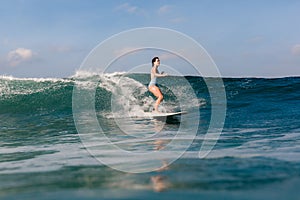 Young woman in bright bikini surfing on a board in ocean