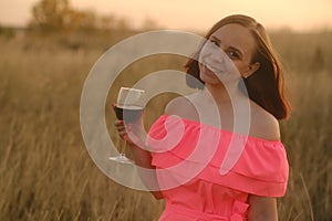 Young woman in bright dress with short hair enjoying fragrance of red wine against sky on sunset.