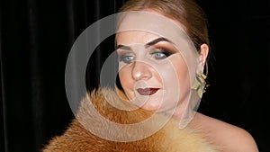 A young woman with bright evening make-up, smoky eyes and long false eyelashes and dark lipstick on her lips poses in