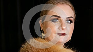 A young woman with bright evening make-up, smoky eyes and long false eyelashes and dark lipstick on her lips poses in