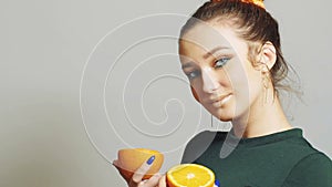 Young woman with bright make-up holds halfs of orange in hands and posing, face of happy girl. Healthy eating concept. Fashionable