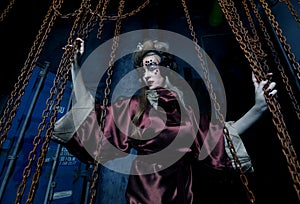 A young woman with bright makeup in a steampunk scenery holds with her hands for red chains.