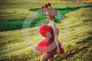 A young woman in a bright red dress with flowers in her hair in autumn field under the blue sky