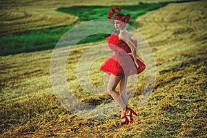 A young woman in a bright red dress with flowers in her hair in autumn field under the blue sky