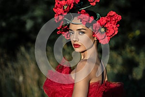 A young woman in a bright red dress with flowers in her hair in autumn field under the blue sky