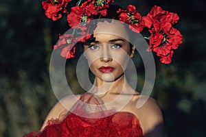 A young woman in a bright red dress with flowers in her hair in autumn field under the blue sky