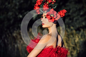 A young woman in a bright red dress with flowers in her hair in autumn field under the blue sky