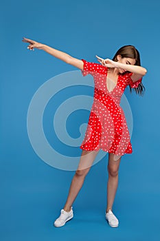 Young woman with bright smile in red casual dress dubbing over blue background.