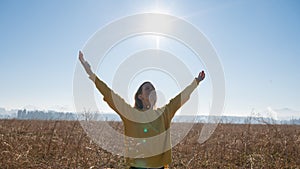 Young woman in bright yellow sweater enjoying life with her arms lifted high