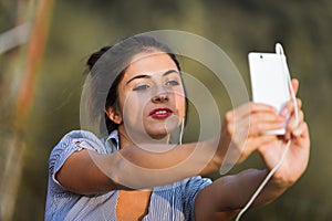 Selfie-taking woman, white phone, wired earphones, park