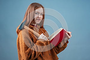 a young woman in a brown jacket smiles holding a hammer in one hand and a book in the other