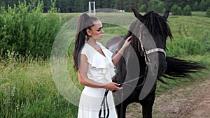 Young woman brunette with hair in ponytail pets black horse