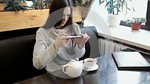 Young woman brunette pictures of teapot and Cup in a cafe on her cell phone. Front view.