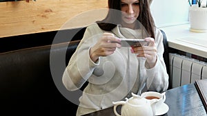 Young woman brunette pictures of teapot and Cup in a cafe on her cell phone. Front view.