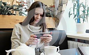 Young woman brunette pictures of teapot and Cup in a cafe on her cell phone. Front view.