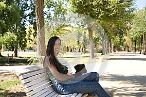 Young woman, brunette, slender, dressed in green t-shirt and jeans, sitting on a bench next to her dog, happy and in a loving