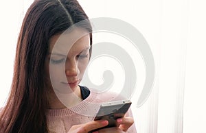 Young woman brunette is typing a message on her mobile phone and looking at screen.