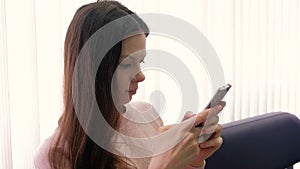 Young woman brunette is typing a message on her mobile phone and looking at screen. Side view.