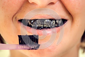 Young woman brushing her teeth with a black tooth paste with active charcoal, and black tooth brush. Close up shot. Healthcare and