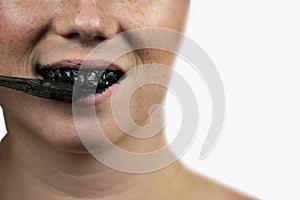 Young woman brushing her teeth with a black tooth paste with active charcoal, and black tooth brush on white background for Teeth