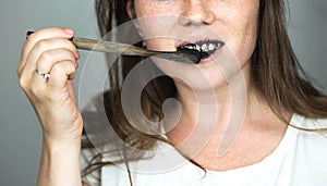 Young woman brushing her teeth with a black tooth paste with active charcoal, and black tooth brush on white background for Teeth