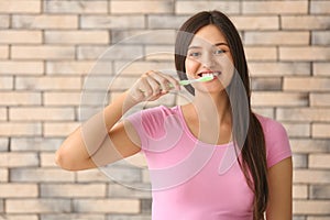 Young woman brushing her teeth on brick wall background