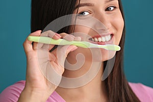 Young woman brushing her teeth on color background