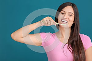 Young woman brushing her teeth on color background