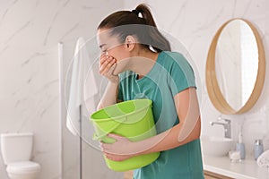 Young woman with bucket suffering from nausea in bathroom. Food poisoning