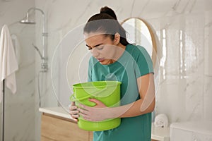 Young woman with bucket suffering from nausea in bathroom. Food poisoning