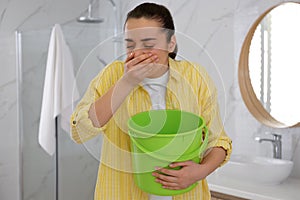 Young woman with bucket suffering from nausea in bathroom. Food poisoning