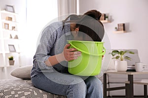 Young woman with bucket suffering from nausea at home. Food poisoning