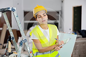 Young woman builder checking documentation in construction site
