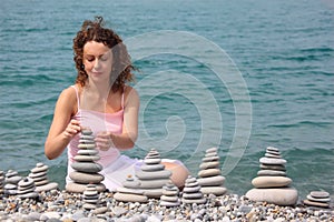 Young woman builds stone stacks on pebble beach