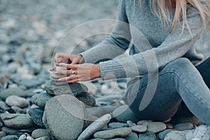 Young woman builds stone stacks pyramid on pebble beach