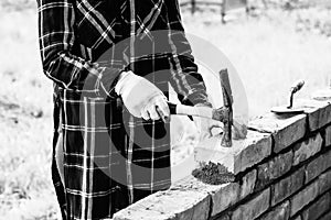 Young woman builds a wall of bricks, lays a brick on a cement-sand mortar, tapping a brick with a hammer