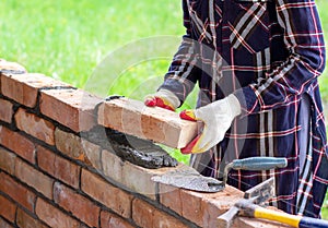 Young woman builds a wall of bricks, lays bricks on cement-sand mortar.