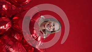 Young woman with bunch of balloons having fun on red background.