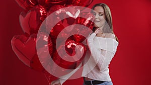 Young woman with bunch of balloons having fun on red background.