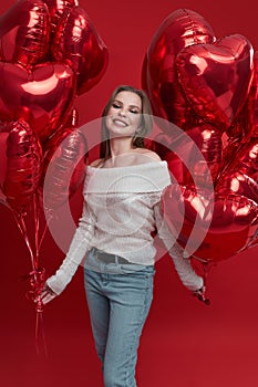 Young woman with bunch of balloons having fun on red background.