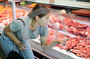 Young woman buyer chooses beef in butcher shop