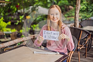 Young woman in a cafe shows a sign - I don't need a straw. No plastic. Global environmental protection issue