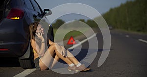 A young woman call on the phone, a broken car on the road in the frame on the emergency