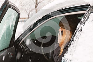 Young woman calling for help or assistance inside snow covered car.  Engine start in frost. Breakdown services in the winter