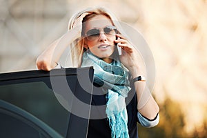 Fashion business woman in sunglasses calling on cell phone by car