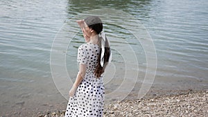 Young woman came out to shore of lake and is looking for someone with her eyes and points her finger there