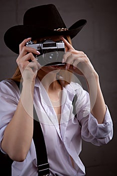 A young woman with a camera. Blonde photographer in white shirt on black sofa