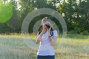 Young woman with camera lens. A beautiful brunette photographer is taking pictures in nature on a summer day